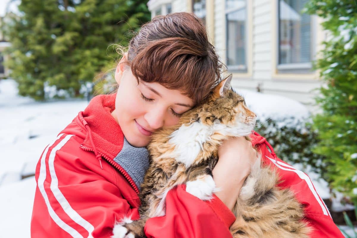 A young woman hugging a fluffy maine coon.