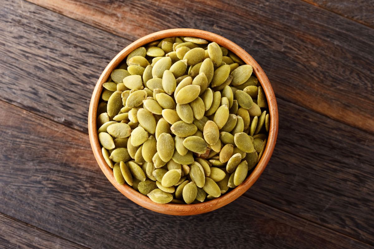 A wooden bowl full of pumpkin seeds on a table.