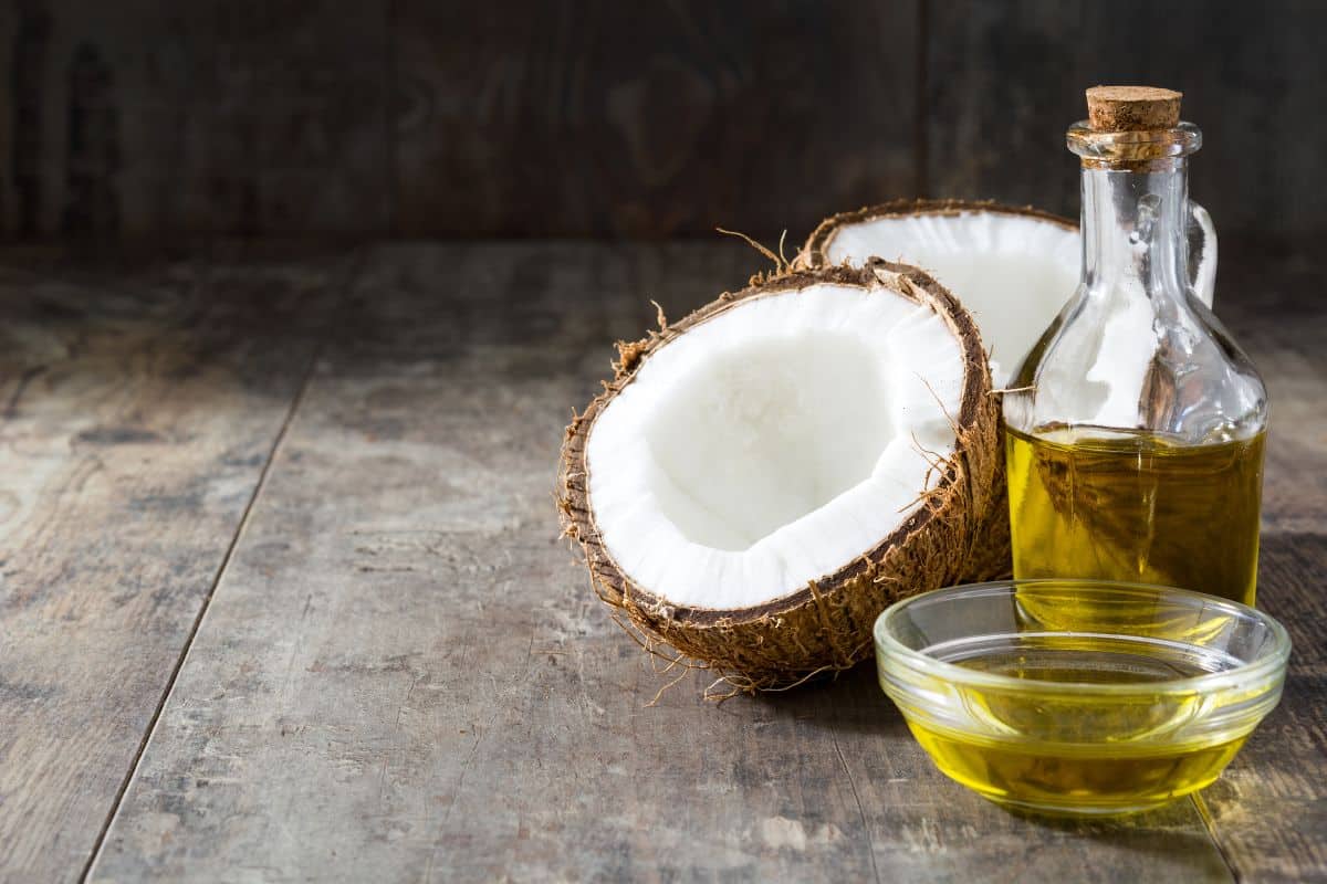 A jar,and a bowl of coconut oil on a table with who half of coconut.