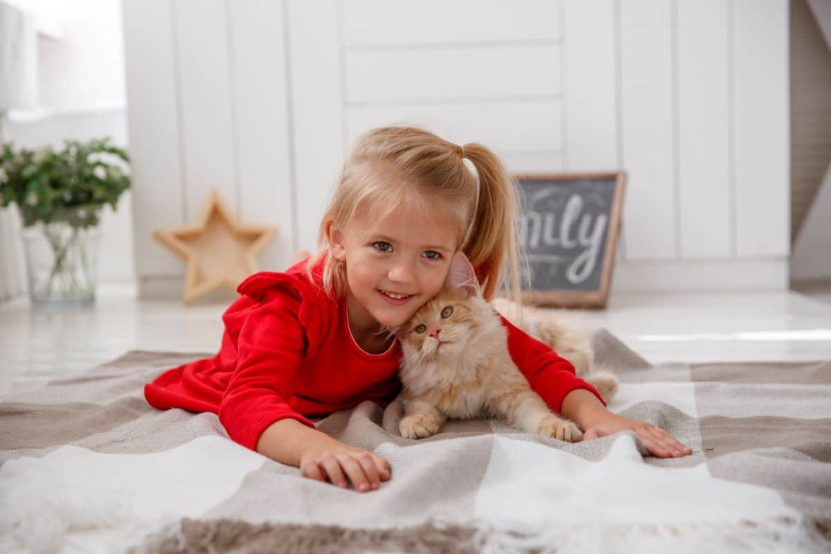 A young girl and a ginger maine coon cat lying on the floor.