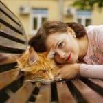 A young woman and a ginger maine coon on a outdoor wooden bench,