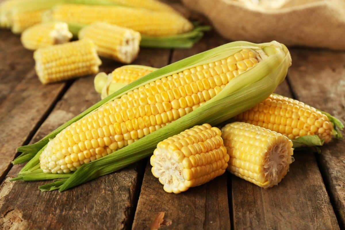 Whole and sliced corn cobs on a wooden table.