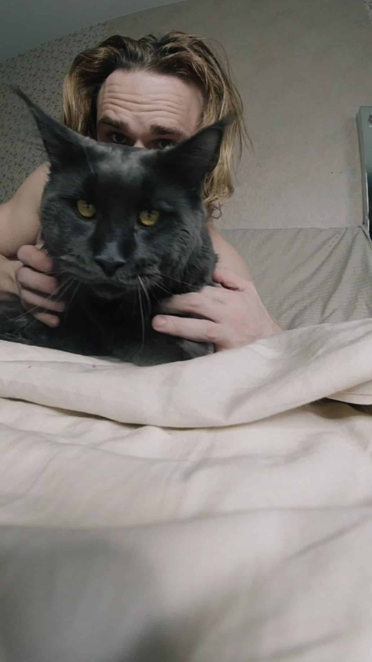 An owner and a black maine coon lying on a bed.