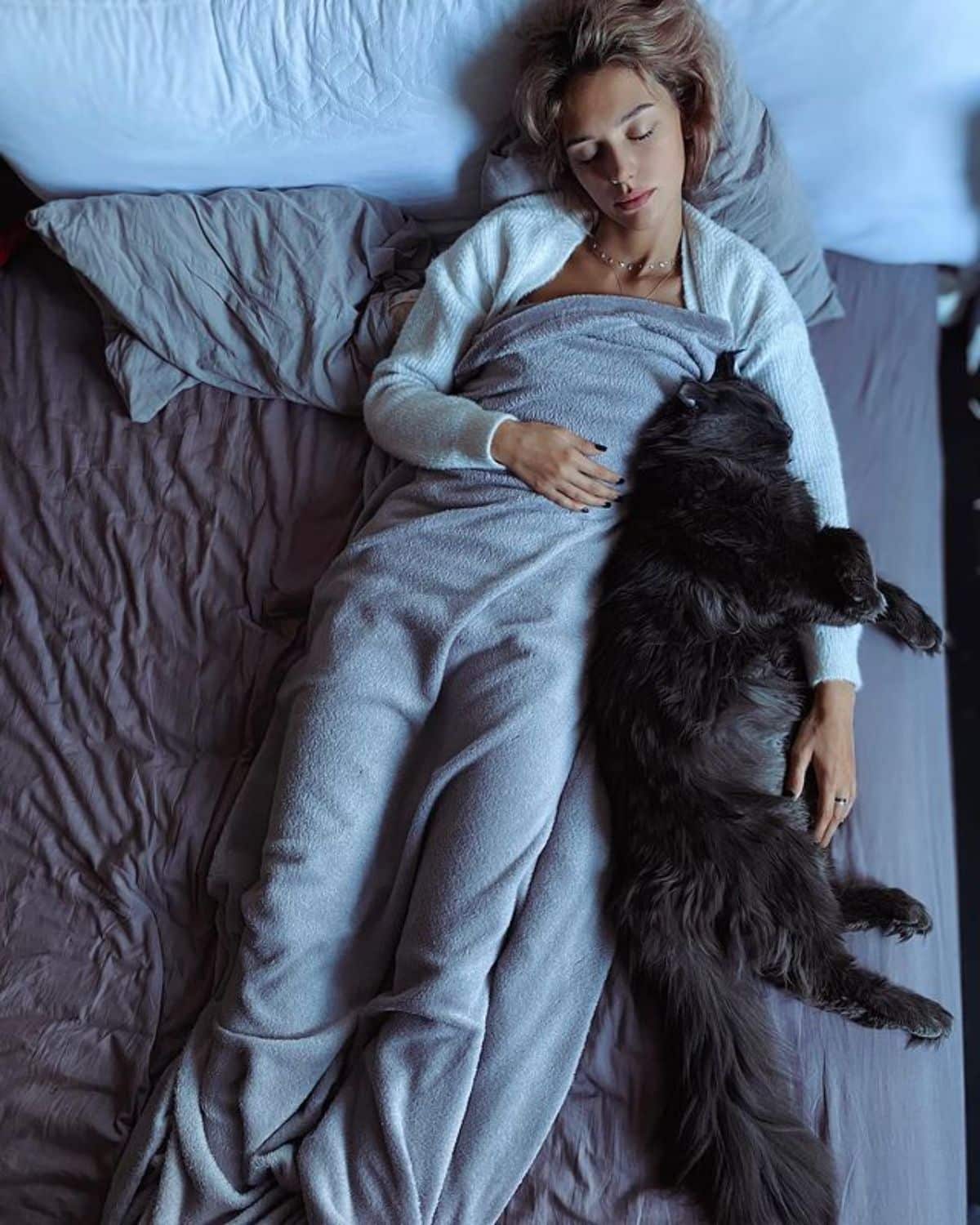 A young woman and a black maine coon sleeping on a bed.