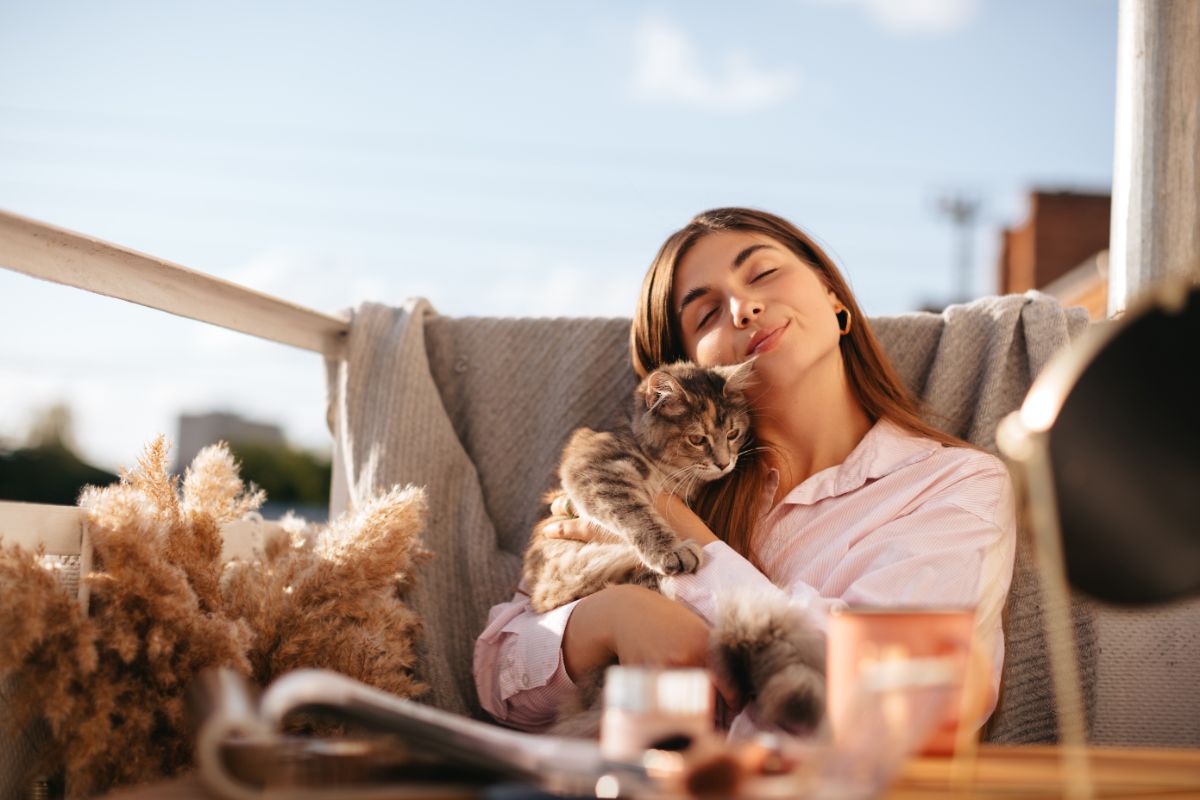 A young woman on a balcony holding a maine coon kitten on a sunny day.