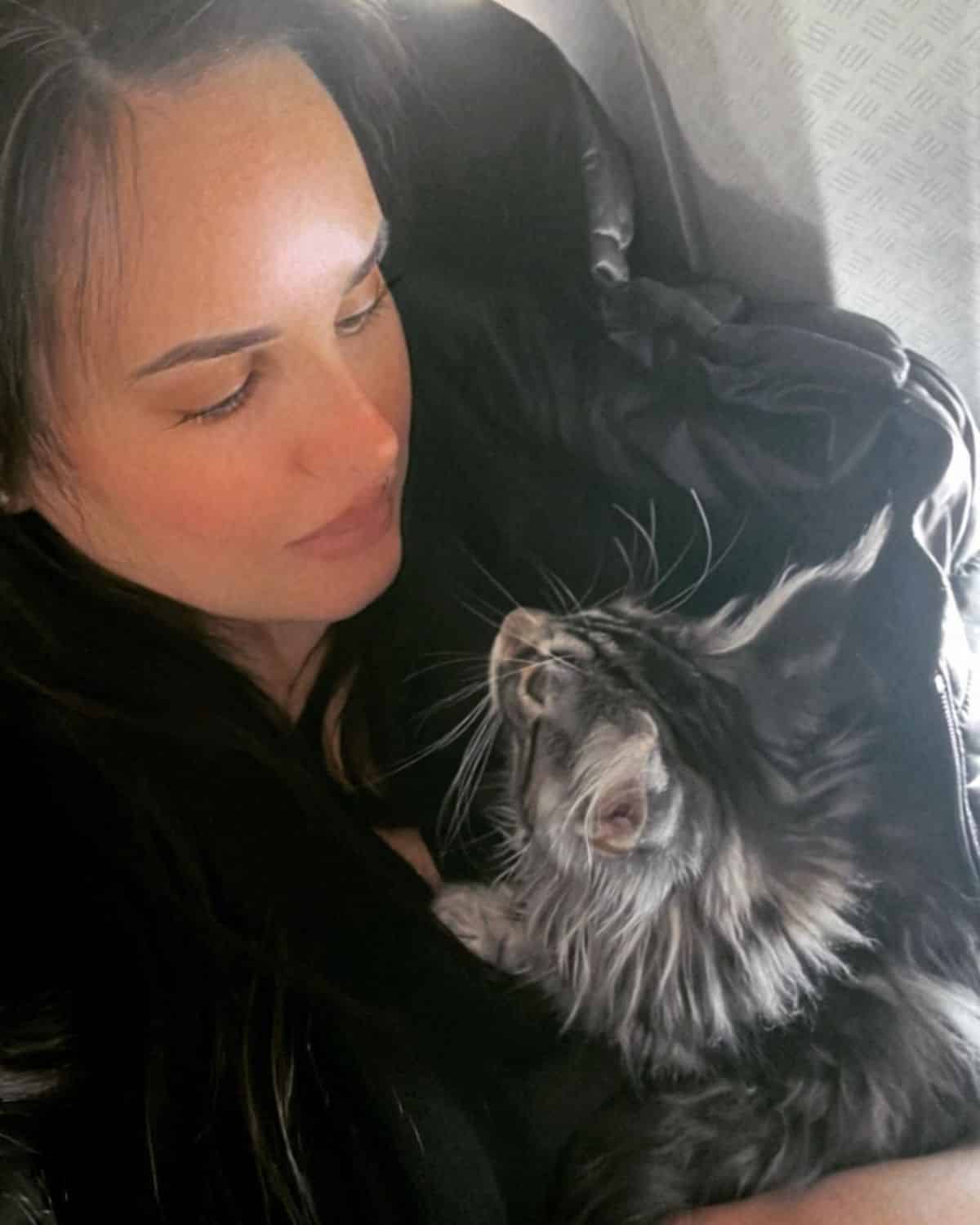 A young woman and a gray maine coon starring into each other eyes.