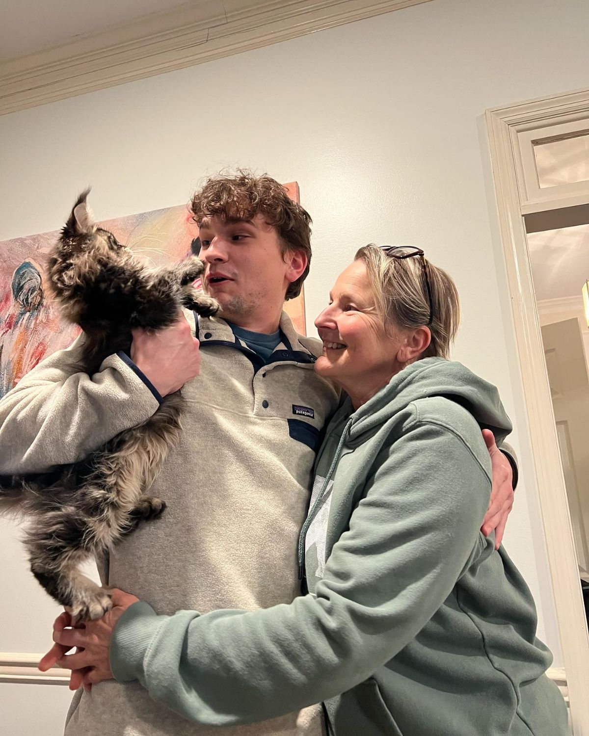 A young man holding his tabby maine coon kitten.