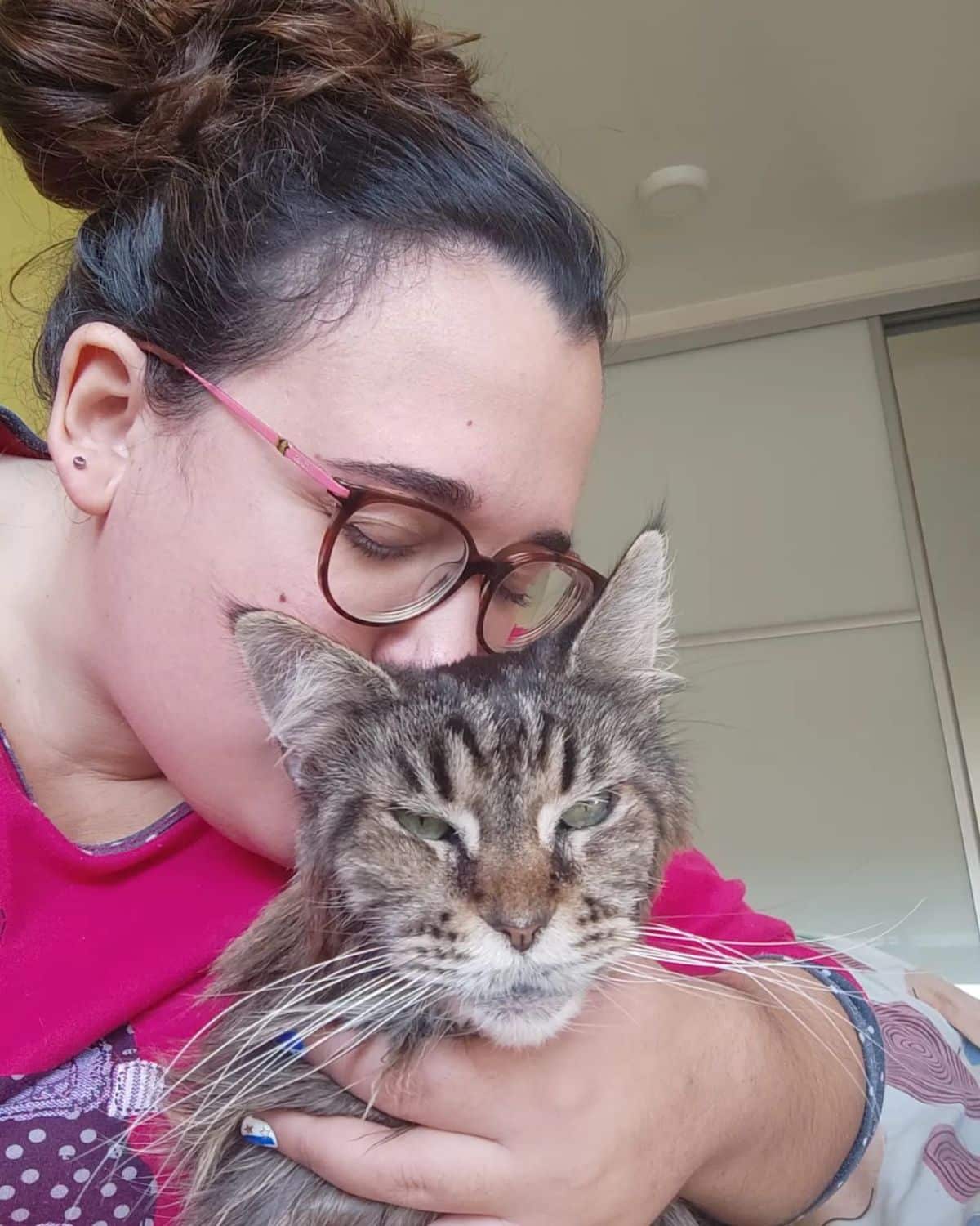 A young woman kissing her tabby maine coon.