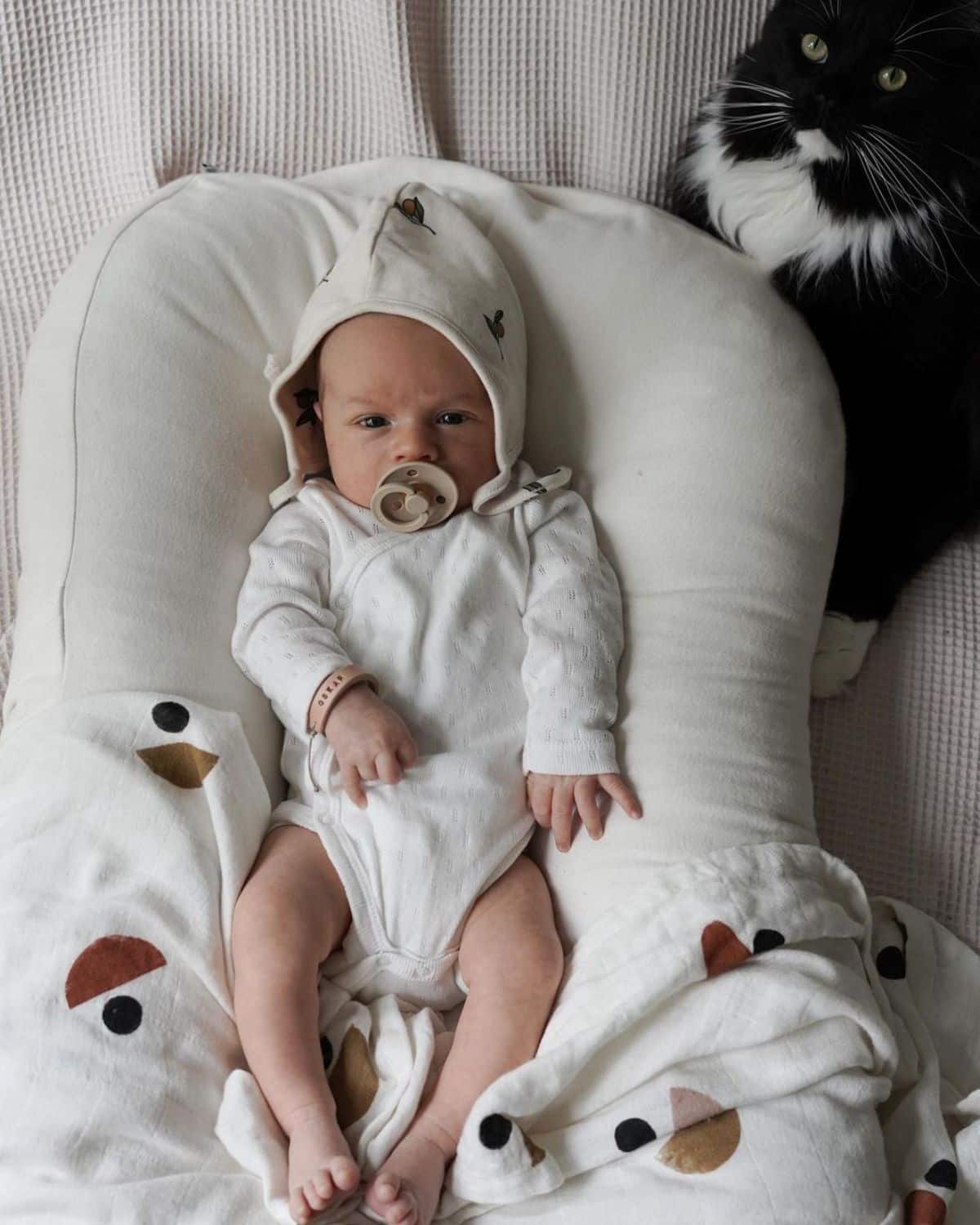 A black-white maine coon guarding a bbaby on a bed.