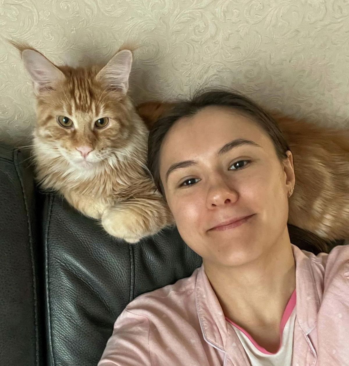 A young woman and her red maine coon sitting on a couch.