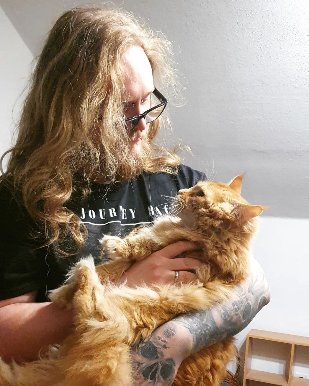 A young man holding and petting a red maine coon.